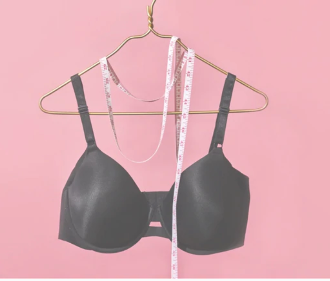 Black bra on a hanger with a measuring tape against a pink background